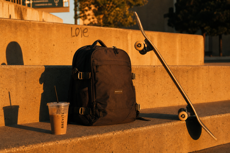 A backpack and skateboard on concrete stairs with a drink.