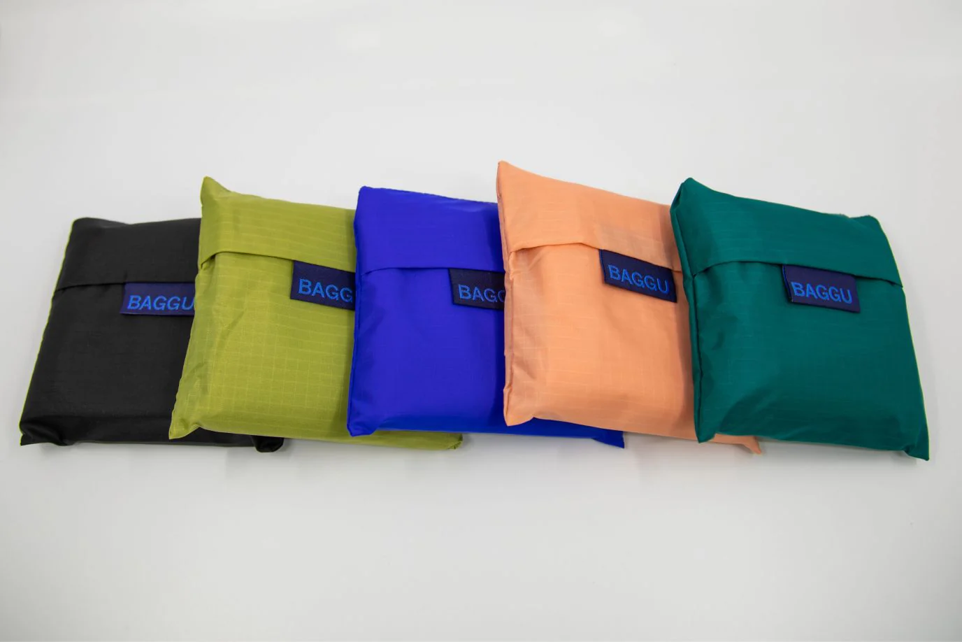 Five colorful reusable bags by Baggu arranged on a white surface.