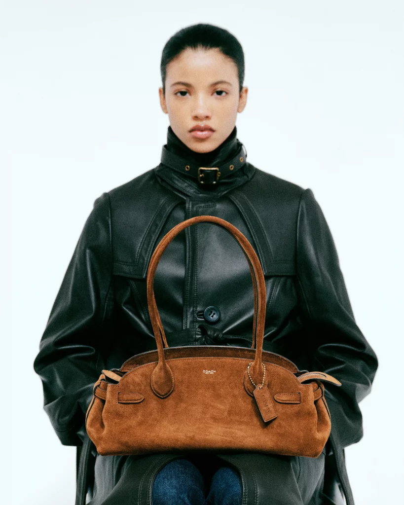 A model sitting with a fashion handbag, wearing a black leather coat.