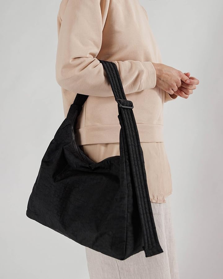A person holding a black bag while dressed in a light-colored sweatshirt.