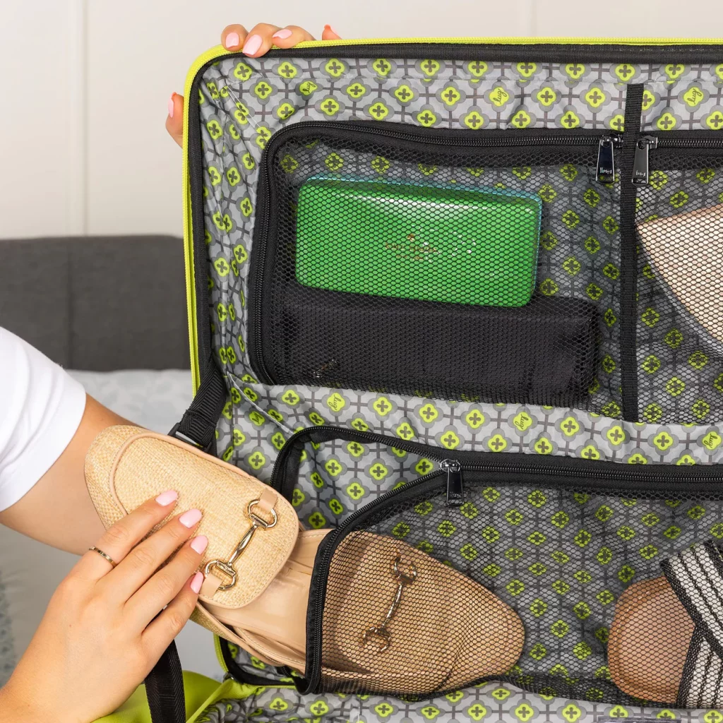 A close-up of a person's hand organizing shoes and a green clutch in a suitcase.