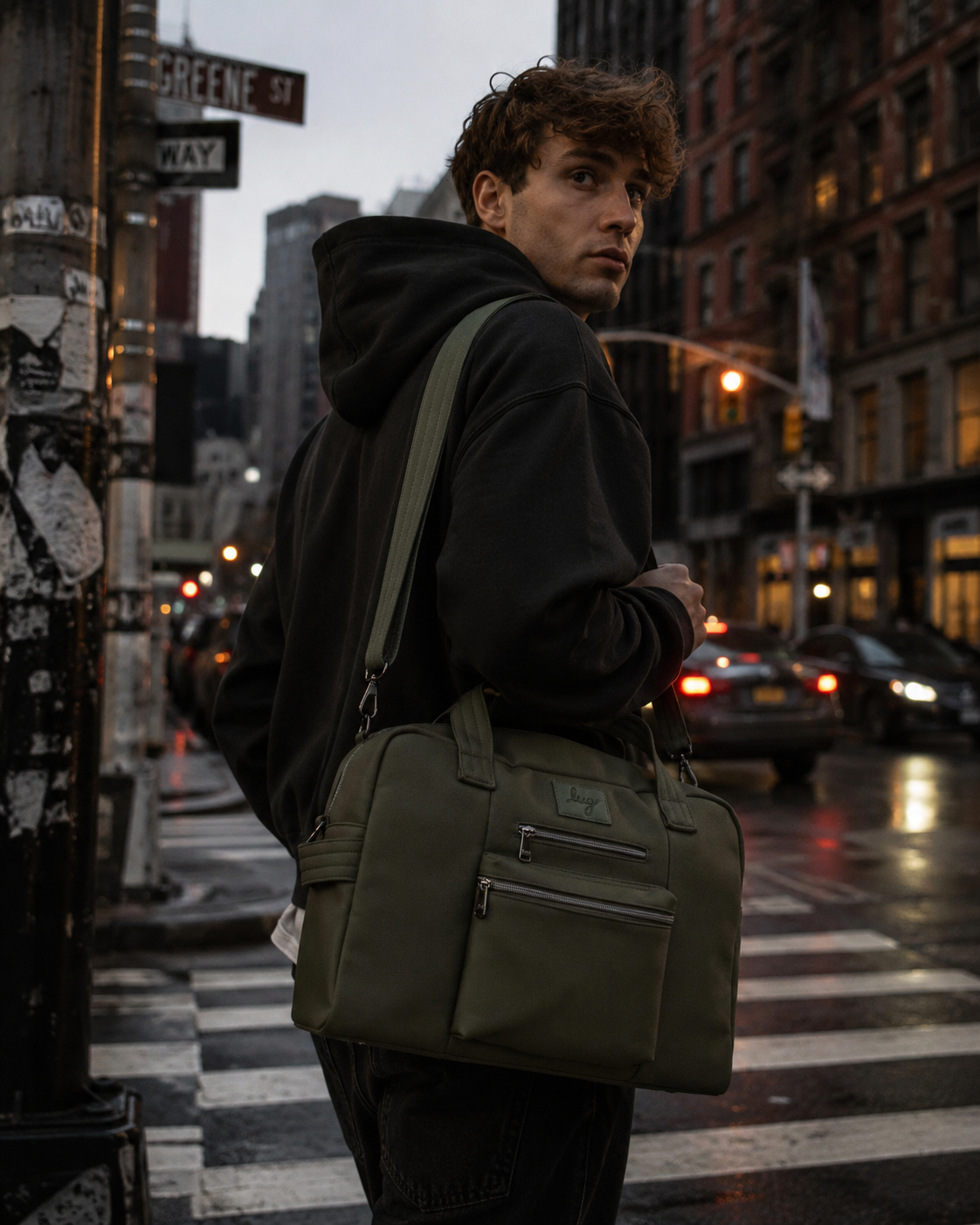 A man standing on a city street at dusk, holding a bag.