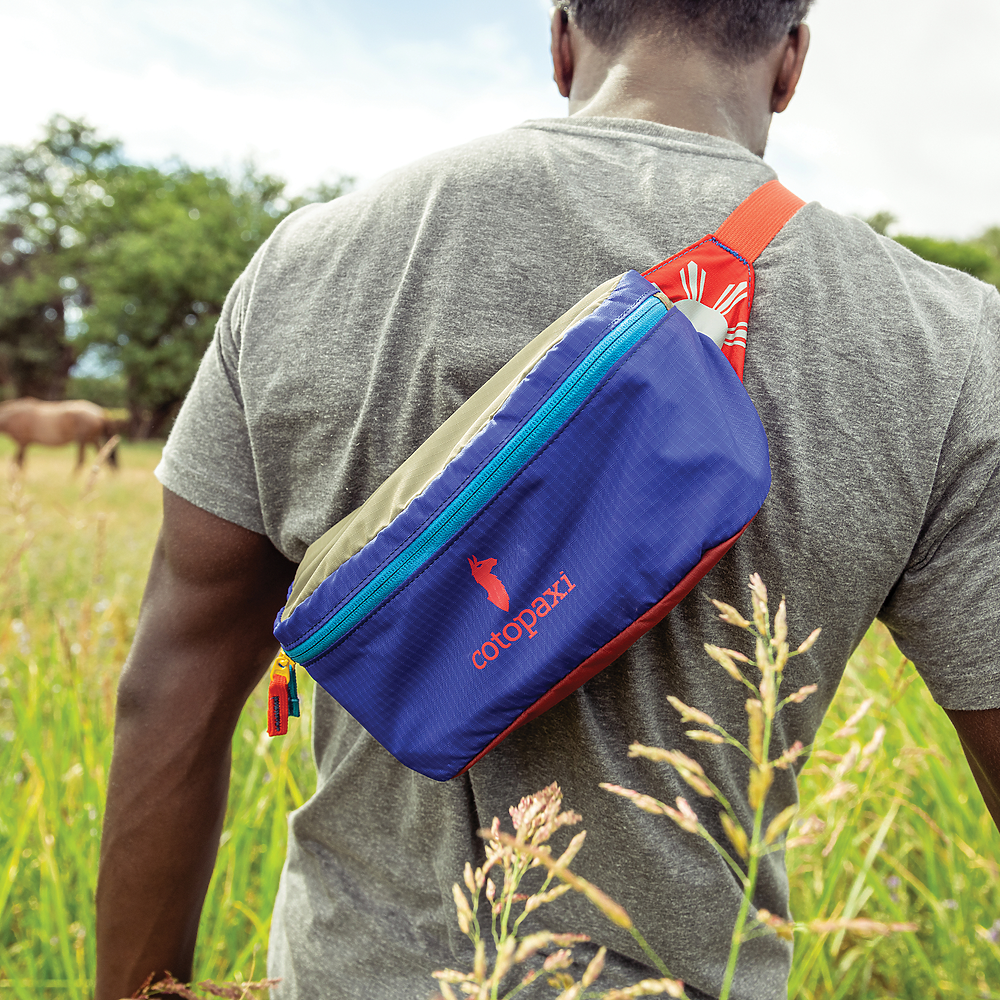 Person wearing a colorful bag in a grassy field.