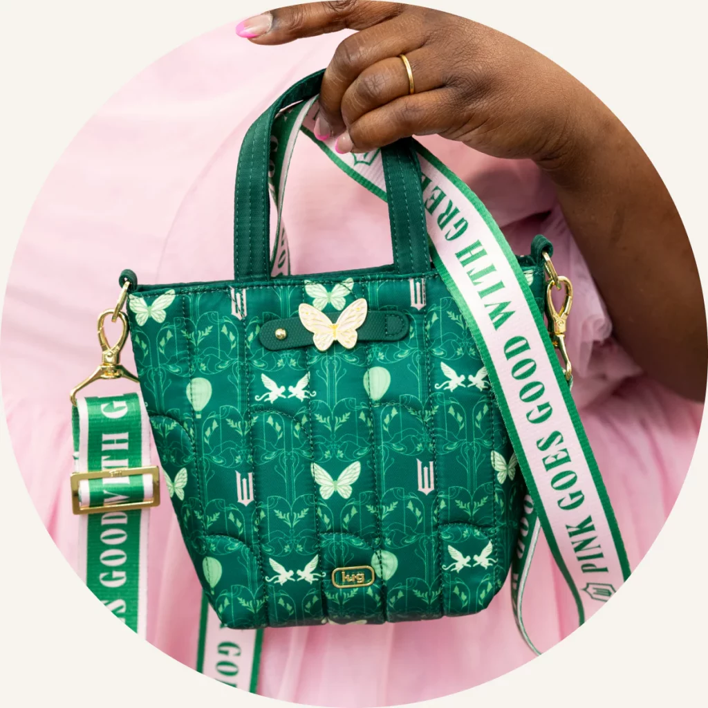 A person holding a green quilted handbag with butterfly designs and a decorative strap.