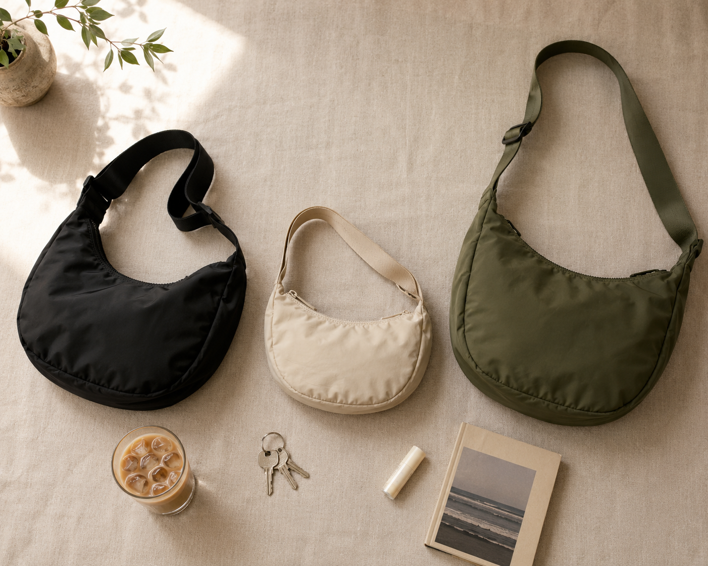 A stylish collection of three shoulder bags in black, beige, and green, with a glass of iced coffee and keys on a beige surface.