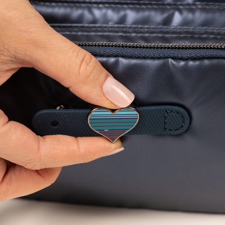 A hand holding a blue heart-shaped zipper pull on a navy bag.